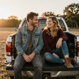 Dave and Carla, a couple sitting on a pickup truck tailgate at sunset, a MileDating trucker dating success story
